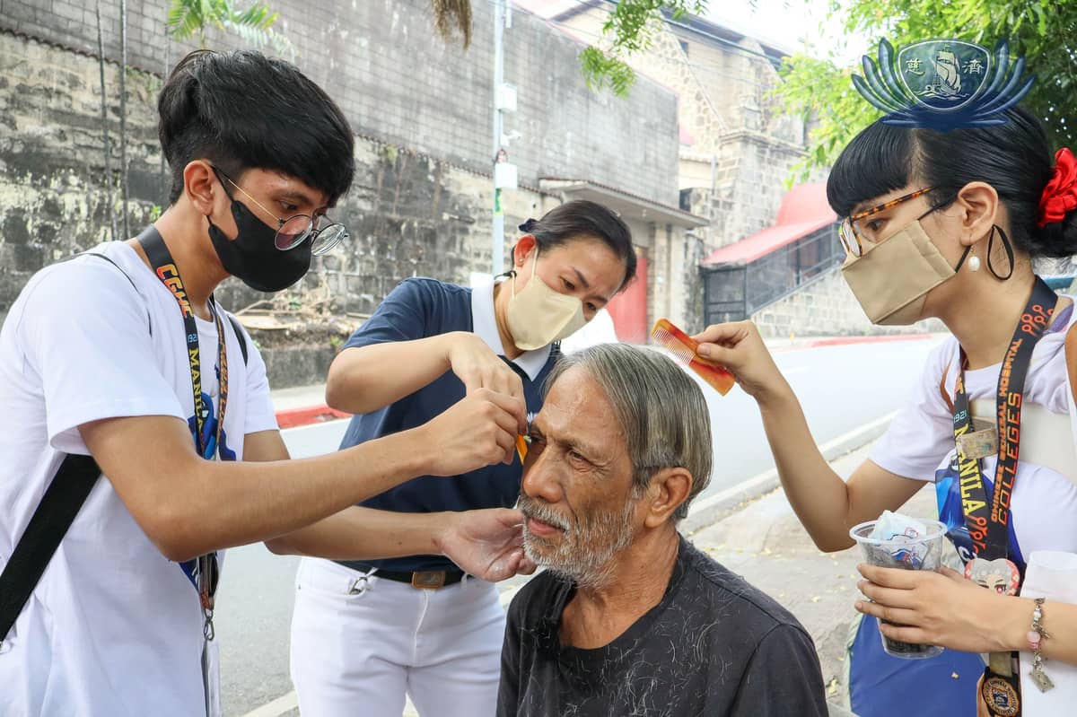 freshmen Psychology students of CGHC and a Tzu Chi volunteer give eye patient Alfonso Simon a haircut before his cataract surgery.